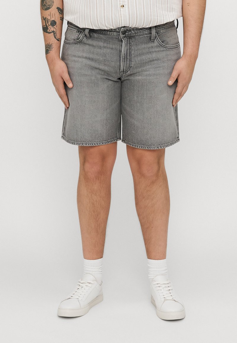 Shorts din denim gri cu croială dreaptă, dotate cu un talie standard și bucle pentru curea, expuse deasupra unor pantofi sport albi și șosete de tip crew.