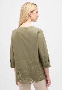 Olivenfarvet tunika med 3/4 ærmer, rund halsudskæring og detaljeret blomsterbroderi i kanten med blonder trim.