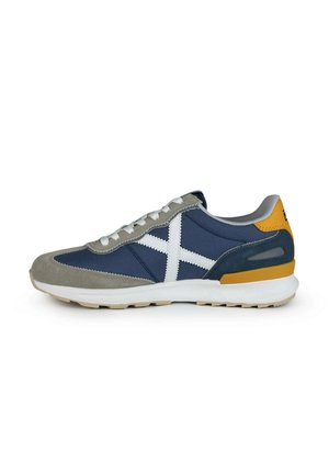 Zapatillas de gamuza y tela en color marino con acentos blancos, parte frontal gris, talón amarillo y suela acolchada. Los cordones son blancos y tienen un diseño de caña baja.