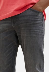 Dunkelgraue Jeans aus Denim mit geradem Schnitt, feiner Textur und Seitentaschen. Kombiniert mit einem korallenfarbenen Kurzarmhemd.