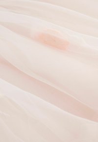 Soft, translucent pale pink fabric with gentle folds and a subtle peach-colored detail visible underneath the layered material.