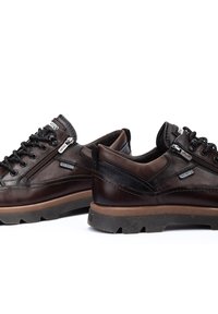 Zapatos de cuero marrón con una superficie texturizada, diseño de cordones, cremallera lateral y suela de goma gruesa. Presentan acentos y detalles de costura en negro.