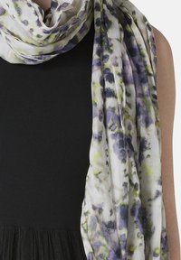 Let scarf i let materiale med et blomsterdesign i lilla og gul på en hvid baggrund, draperet over en sort struktureret top.