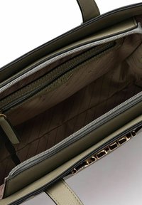 Interior de un bolso verde oliva con un bolsillo con cremallera, textura de cuero suave, forro con patrón y detalles de hardware en tono dorado.