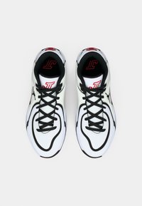 Λευκά και μαύρα αθλητικά παπούτσια με κόκκινες λεπτομέρειες και μαύρα κορδόνια, με θέα από πάνω σε άσπρο φόντο.