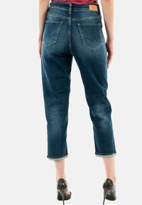 Jeans en denim bleu avec une coupe ajustée, longueur raccourcie et ourlets retroussés. Présente deux poches arrière avec un motif de couture distinct.