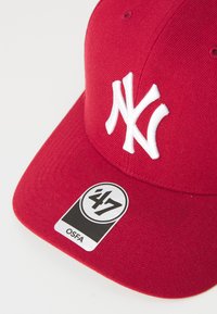 Casquette de baseball rouge en tissu avec une forme structurée. Présente un logo "NY" en relief en blanc et une étiquette noire avec "47" et "OSFA."
