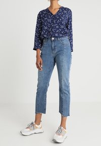 Navy blouse with white floral pattern, button-down front; light blue denim jeans with frayed hem; white and gray sneakers with accents.