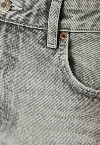 Gray acid-wash denim jeans close-up showing front pocket, belt loop, rivets, and metal button with detailed stitching.