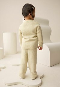 Cream-colored knitted sweater and pants set, featuring a ribbed hem, textured fabric, and relaxed fit, worn by a child from the back.