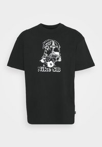 Czarna koszulka z białym graficznym wzorem palmowego drzewa i wózka golfowego, z napisem "Nike SB" poniżej ilustracji.