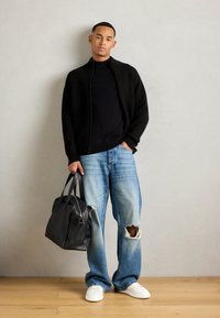 Veste en maille noire à col zip, t-shirt noir, jeans déchirés bleu clair, baskets blanches et sac fourre-tout en cuir noir avec fermeture éclair.
