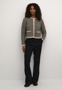 Sort og creme ternet strikcardigan med rund hals, frontknapper og to lommer. Modellen bærer sorte bukser og sko.