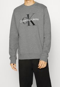 Gray crewneck sweatshirt made of soft fabric, featuring a black "CK" logo and "Calvin Klein Jeans" text on the front. Relaxed fit.