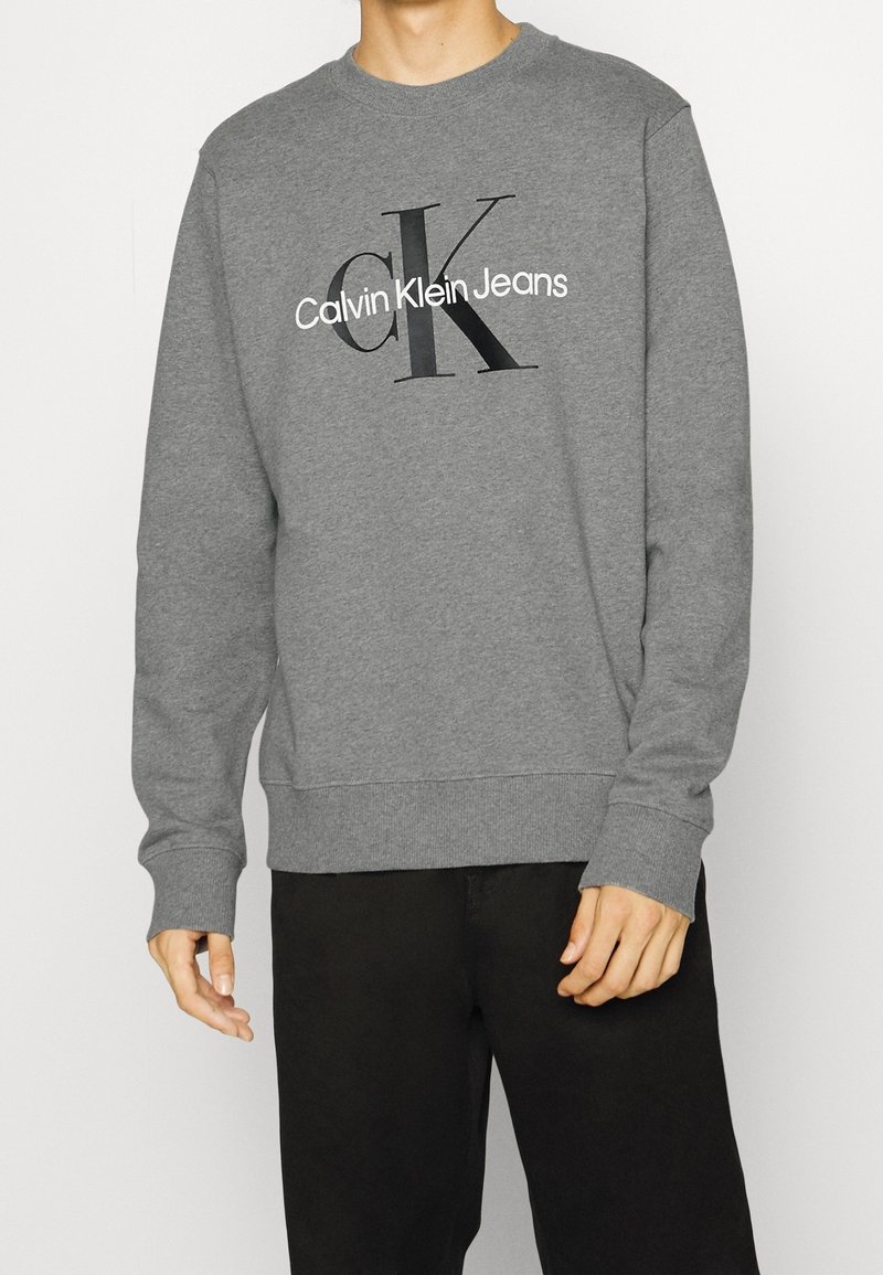 Gray crewneck sweatshirt made of soft fabric, featuring a black "CK" logo and "Calvin Klein Jeans" text on the front. Relaxed fit.