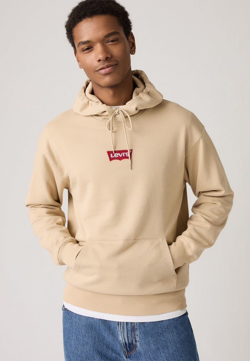 Beige hooded sweatshirt made of cotton, featuring a front pocket and red Levi's logo patch. Casual fit with ribbed cuffs and hem.