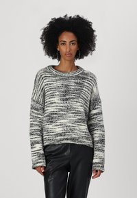 Strikket genser i svart og hvite striper, med bred rund hals, lange ermer og teksturert overflate. Kombinert med svarte bukser i faux skinn.