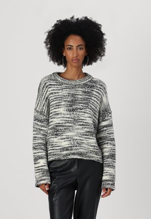 Pull en tricot à rayures noires et blanches, avec un col rond large, des manches longues et une finition texturée. Associé à un pantalon en faux cuir noir.