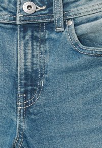 Close-up af blå denimjeans, der viser frontlomme, bæltestrop, dobbeltsyning og metal knap med mærkenavnet Pull&Bear.