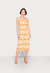 Vestido midi floral laranja com decote quadrado e alças finas. Apresenta um padrão de flores brancas e uma silhueta reta. Acentuado com sandálias de salto laranja.