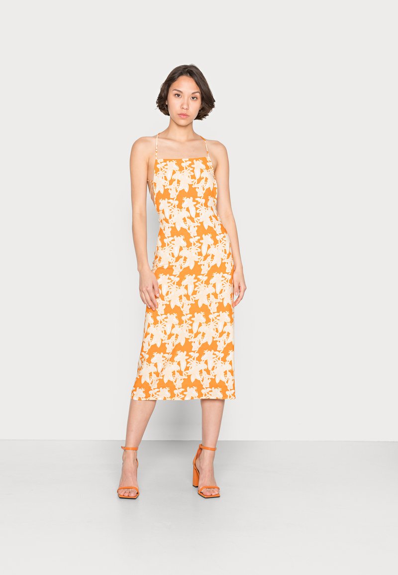 Vestido midi floral laranja com decote quadrado e alças finas. Apresenta um padrão de flores brancas e uma silhueta reta. Acentuado com sandálias de salto laranja.