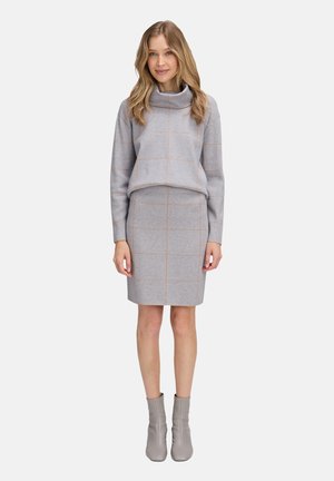 Grauer cropped Pullover mit einem Schalkragen und beigem Karomuster, kombiniert mit einem taillierten grauen Rock und grauen Knöchelstiefeln.