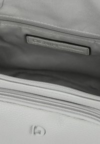 Interno di una borsa in pelle bianca con una fodera in tessuto grigio liscia, dotato di una tasca con zip e un'etichetta in pelle con il logo.