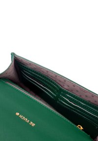 Green wallet with multiple card slots and a zippered compartment, featuring a textured exterior and a polka dot inner lining. Gold logo detail included.