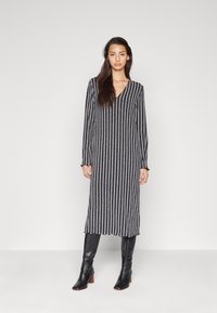Robe rayée avec un décolleté en V, des manches longues et une coupe mi-longue en noir, blanc et gris. Texture douce avec un ourlet évasé. Bottes noires jusqu'aux genoux.