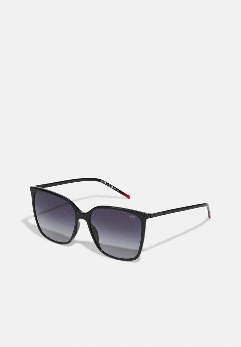 Gafas de sol negras en forma de cuadrado con lentes gris degradado. Patillas delgadas y elegantes con acentos rojos. Marca mínima en la lente.