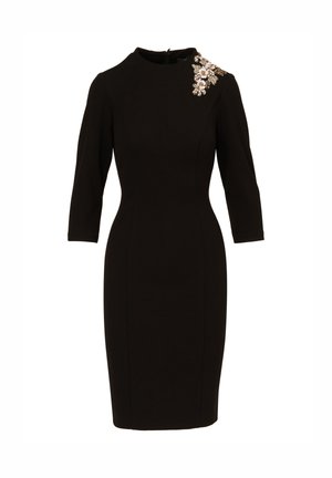 Zwart aansluitend jurk met driekwart mouwen, ronde halslijn en een decoratieve bloemenversiering op de linker schouder.
