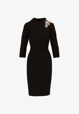 Zwart aansluitend jurk met driekwart mouwen, ronde halslijn en een decoratieve bloemenversiering op de linker schouder.