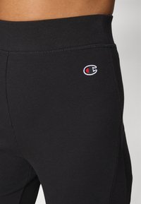 Leggings neri a coste con vita alta, caratterizzati da un piccolo logo ricamato in rosso e bianco sul lato per dettagli e branding.