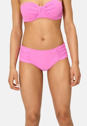 Mujer con un top de bikini sin tirantes rosa y bragas de bikini a juego de talle alto con fruncidos a los lados, sobre un fondo liso.