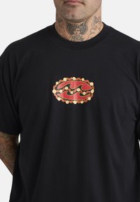 Zwarte katoenen t-shirt met een centrale ovale grafiek in rood en goud, met golfachtige patronen en cirkelvormige accenten, wat een gedurfde uitstraling creëert.