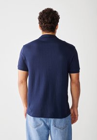Marineblå ribbestrikket polo skjorte med korte ermer, med klassisk krage og rett nederkant, paret med lys blå denimjeans.