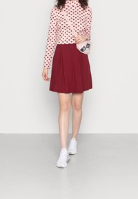 Roze top met lange mouwen en hartjesmotief, gecombineerd met een bordeauxroze geplooide rok en witte sportieve sneakers. Kleine roze schoudertas als accent.