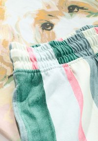 Kokvilnas šorti ar zaļām, rozā un baltām svītrām, elastīgu jostasvietu un mīkstu tekstūru, fona attēlā krāsaina suņa ilustrācija.