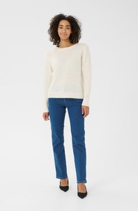 Pull léger en tricot crème avec col rond, poignets et ourlet côtelés ; associé à un jean bleu droit et des escarpins noirs à bout pointu.