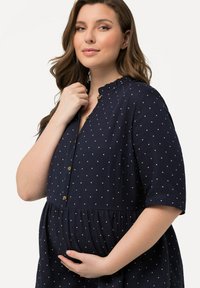 Abito premaman blu navy con pois bianchi, maniche corte, colletto arricciato e bottoni davanti, progettato per il comfort.