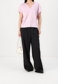 Top rosa a scollo a V con maniche corte, abbinato a pantaloni neri a gamba larga e una borsa bianca. Il tessuto appare liscio e leggero.