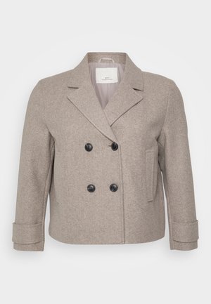 Dobbeltradet jakke i lys beige ullblanding. Har sorte knapper, spiss krage og en enkelt lomme på høyre side.
