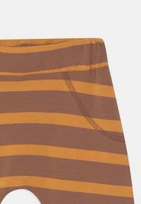 Leggings listrados em castanho e mostarda com uma textura suave, apresentando uma cintura elástica e detalhe de bolso lateral.