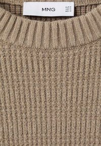 Suéter de punto beige con textura acanalada y cuello redondo. La etiqueta muestra las tallas en EUR, EE. UU. y MEX: EUR M, EE. UU. M, MEX M.