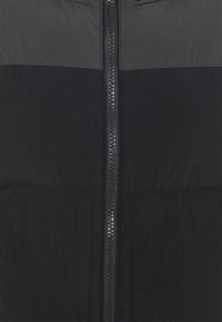 Giacca nera e grigia scura con zip, presenta una texture liscia, due colori e una zip centrale. Include due tasche frontali.