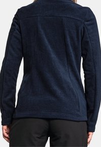 Mörkblå fleecejacka med en texturerad yta, horisontell söm över övre delen av ryggen och tight passform vid ärmar och söm.
