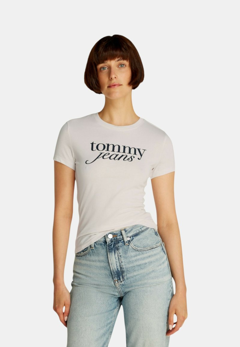 T-shirt bianco a maniche corte con "tommy jeans" stampato in corsivo blu navy. Abbinato a jeans a vita alta blu chiaro.