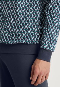 Sweatshirt met een geometrisch patroon van driehoeken in wit, turquoise en zwart. De mouwen zijn effen marineblauw met een gestructureerde afwerking.