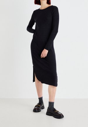 Černé dlouhé žebrované šaty s dlouhým rukávem, kulatým výstřihem a bočním rozparkem. Nošeny se šedými ponožkami a černými masivními mokasínami se zlatými kovovými doplňky.