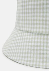 Zaļa un balta ģeometriska viklapa cepure ar plašu malu un teksturētu audumu, ar izšūtu akcentu gar pamatni, lai pievienotu papildus detaļas.